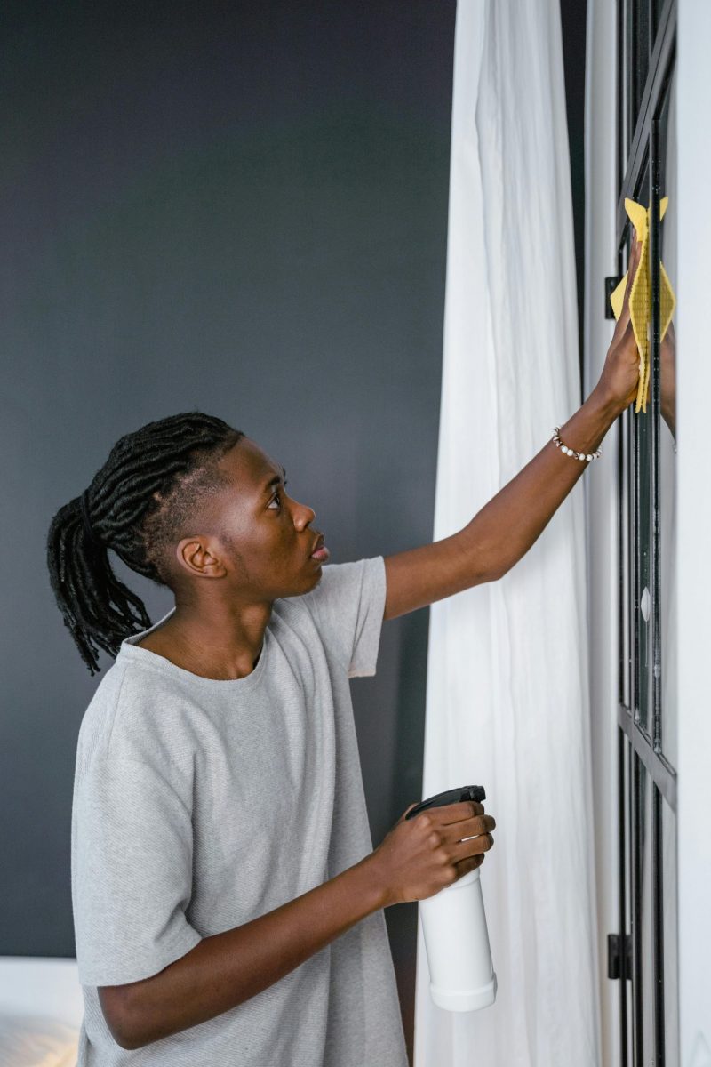 Young adult cleaning a window indoors with a spray bottle and cloth.